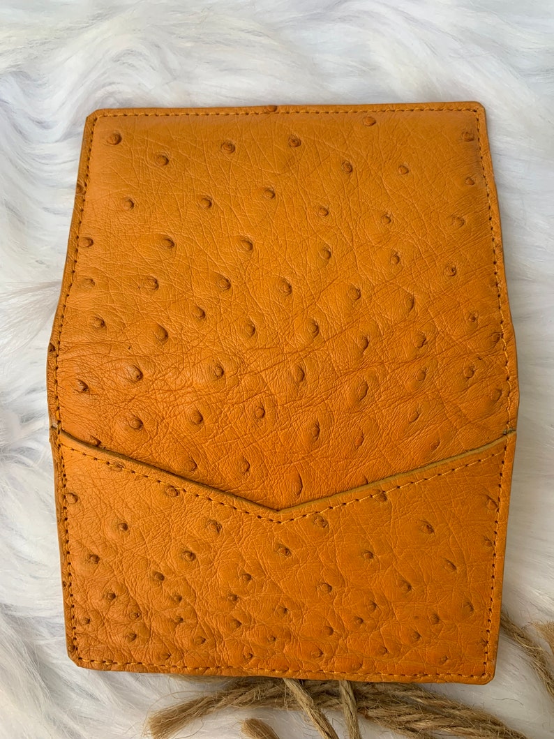 Puede incluir: Una cartera de cuero marr&oacute;n con cierre de solapa y un patr&oacute;n texturizado de piel de avestruz.