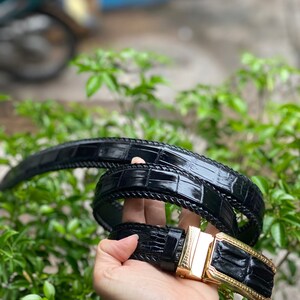 May include: A black leather belt with a gold buckle. The belt is made of crocodile skin and has a textured pattern.