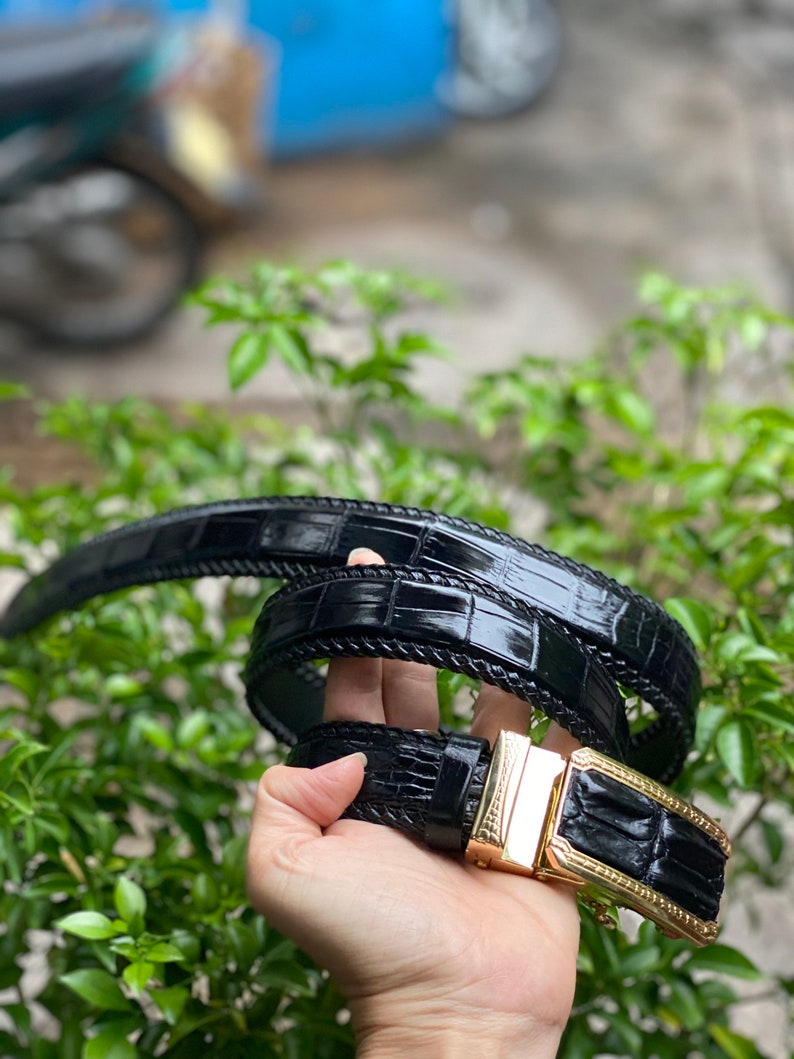May include: A black leather belt with a gold buckle. The belt is made of crocodile skin and has a textured pattern.