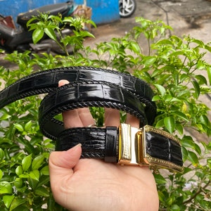 May include: A black leather belt with a gold buckle. The belt is made of crocodile skin and has a braided design.