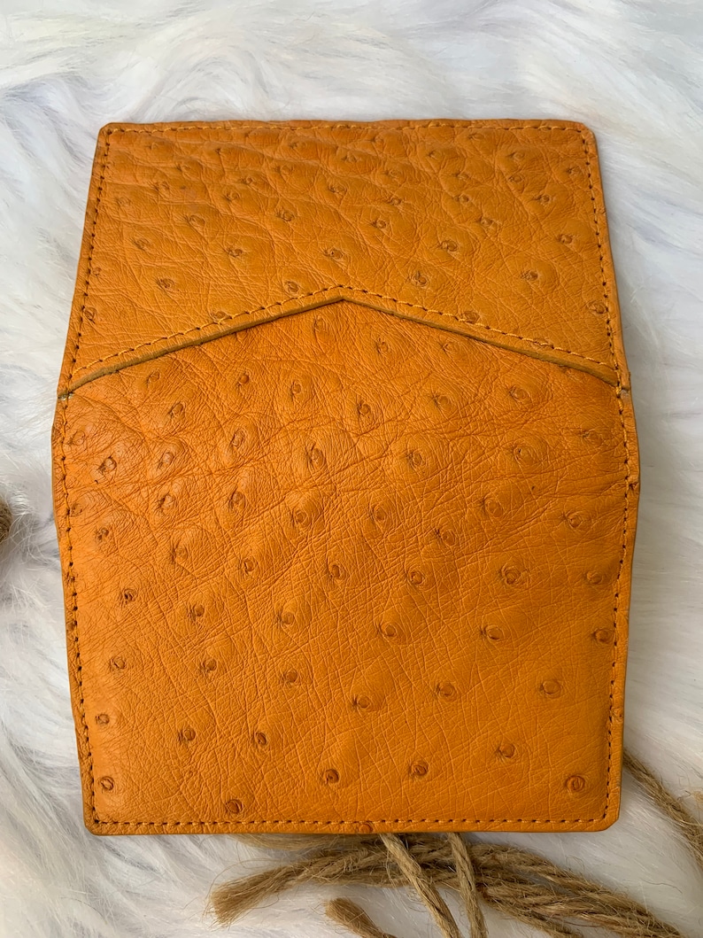 Puede incluir: Una cartera de cuero marr&oacute;n con un patr&oacute;n texturizado de piel de avestruz. La cartera tiene un cierre de solapa y un solo detalle de costura.