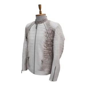 Puede incluir: Chaqueta de cuero blanca con cuello alzado y cierre de cremallera. Los hombros y la parte superior de las mangas presentan un patr&oacute;n texturizado, similar al de un cocodrilo, en color marr&oacute;n claro. La chaqueta tiene dos bolsillos con cremallera y un corte entallado.