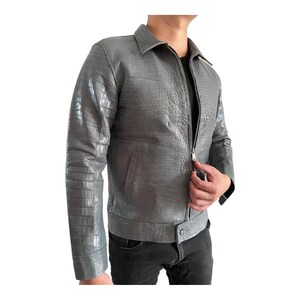 May include: A gray leather jacket with a crocodile skin texture. The jacket has a zipper closure, a collared neckline, and long sleeves. The jacket is a medium gray color and has a classic design.