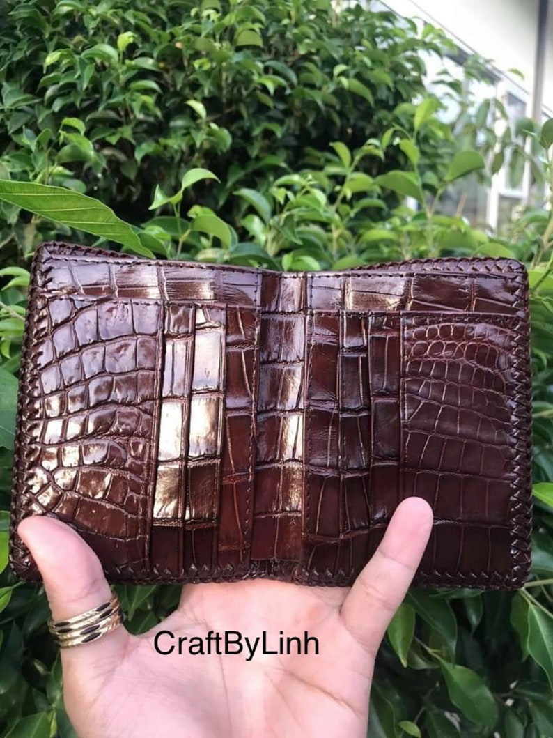 May include: A brown leather wallet with a crocodile pattern and multiple card slots. The wallet is open and the inside is visible. The text "CraftByLinh" is visible on the bottom of the image.