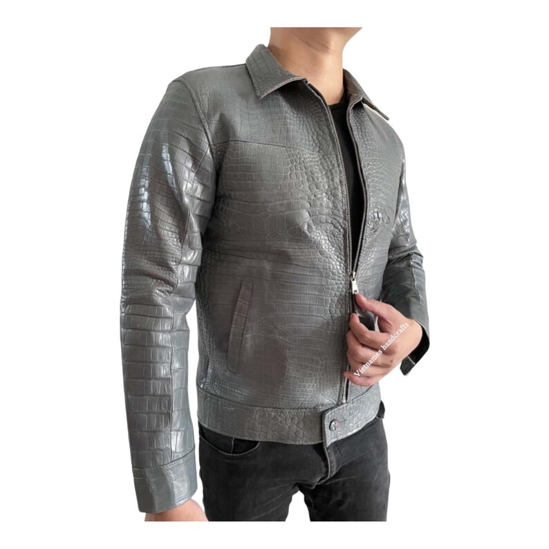 May include: A gray leather jacket with a crocodile skin texture. The jacket has a collared neckline, a zipper closure, and a buttoned waist. The sleeves are long, and the jacket appears to be a medium weight.