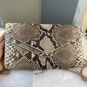 Puede incluir: Un pequeño bolso de mano de piel de serpiente blanco y marrón con cierre de solapa.