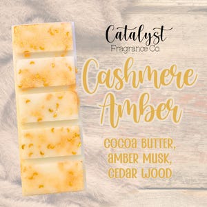May include: A rectangular, off-white wax melt bar with five sections, speckled with gold flecks. The text "Catalyst Fragrance Co." and "Cashmere Amber" are displayed. The scent includes cocoa butter, amber musk, and cedar wood.