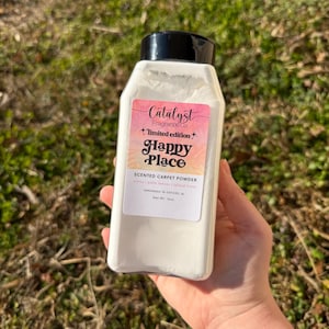 May include: A white rectangular bottle of scented carpet powder with a black lid. The label reads "Catalyst Fragrance Co. + limited edition+ Happy Place." The powder is labeled "Scented Carpet Powder" and is handmade in Oxford, AL. Net Wt. 16oz.