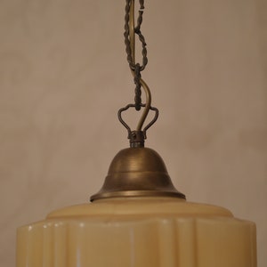 K&ouml;nnte beinhalten: Eine Vintage-H&auml;ngelampe aus Messing mit einem cremefarbenen Glasschirm. Der Schirm hat einen gewellten Rand und eine strukturierte Oberfl&auml;che.