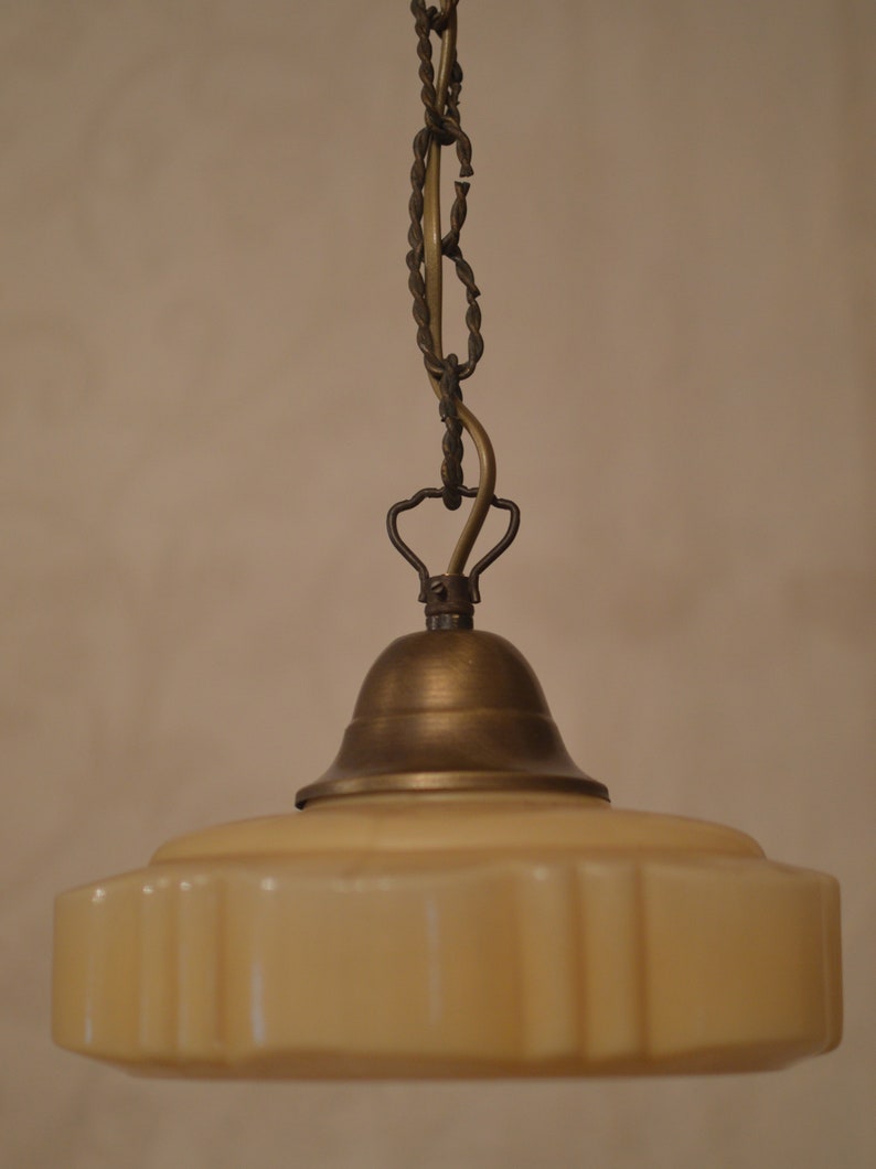 K&ouml;nnte beinhalten: Eine Vintage-H&auml;ngelampe aus Messing mit einem cremefarbenen Glasschirm. Der Schirm hat einen gewellten Rand und eine strukturierte Oberfl&auml;che.