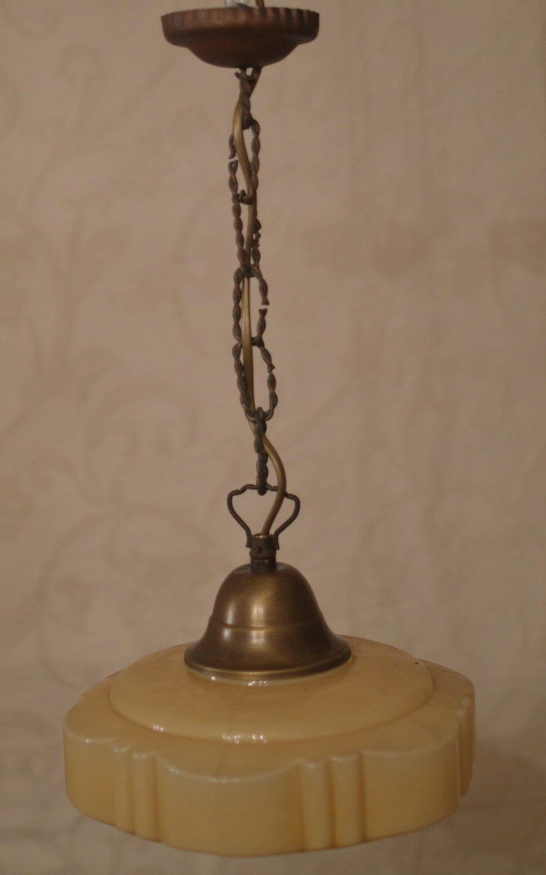K&ouml;nnte beinhalten: Eine Vintage-H&auml;ngelampe aus Messing mit einem cremefarbenen Glasschirm. Der Schirm hat einen gewellten Rand und ein dekoratives Muster.