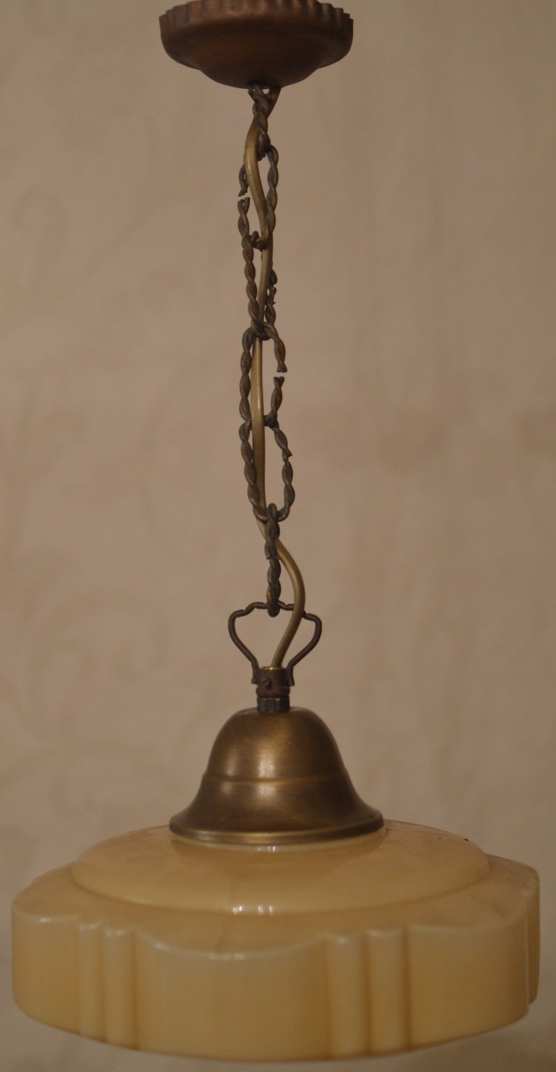 K&ouml;nnte beinhalten: Eine antike Deckenleuchte aus Messing und Glas mit einem cremefarbenen Glasschirm. Der Schirm hat einen gewellten Rand und ein dekoratives Muster.