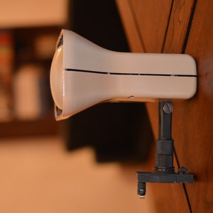 Puede incluir: Un foco vintage blanco con una base de metal negro y un brazo ajustable. El foco tiene un reflector redondo blanco y una carcasa de metal negro.