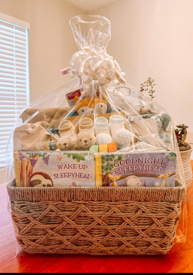 May include: A wicker basket filled with baby gifts, including a plush toy, socks, and two board books titled "Wake Up Sleepyhead" and "Goodnight Sleepyhead".