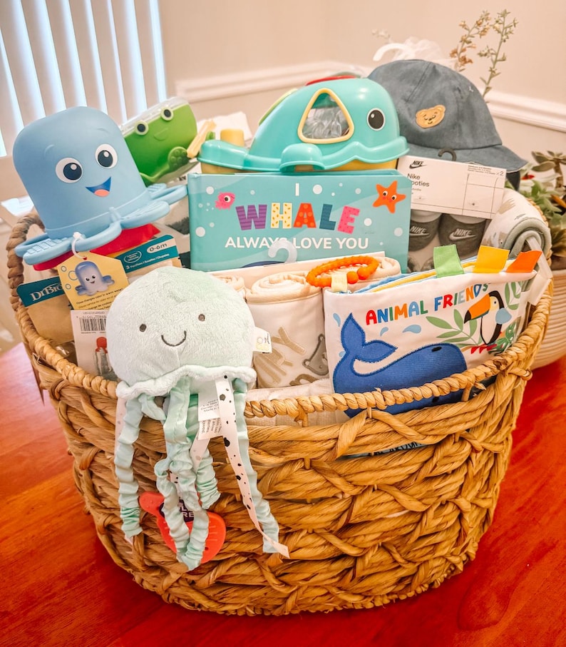 May include: A wicker basket filled with baby shower gifts, including a blue and green whale toy, a blue and white octopus toy, a blue and white jellyfish toy, a book titled "I Whale Always Love You", a blue and white animal friend book, and a pair of blue and white Nike socks.