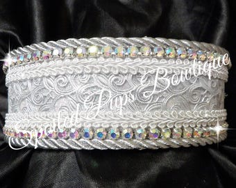May include: A white collar featuring a central band of intricate floral lace, bordered by two rows of twisted silver cord and two rows of iridescent, multi-colored rhinestones. The text Spoiled Pups Boutique is overlaid across the center.