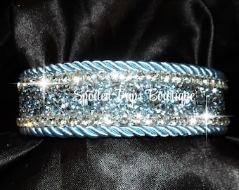 May include: A light blue dog collar with three rows of clear and light blue rhinestones. The collar has a rope-like design and the text "Spoiled Pups Boutique" is visible in the center.