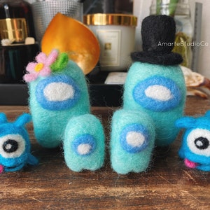 K&ouml;nnte beinhalten: Ein Set aus f&uuml;nf Filzspielzeugen, darunter zwei blaue Filzfiguren mit H&uuml;ten, eine blaue Filzfigur mit einer Blume und zwei kleinere blaue Filzfiguren. Die Figuren sind alle in Form einer Person mit einem runden Kopf und einem kleinen K&ouml;rper. Die Spielzeuge sind alle handgefertigt und haben ein skurriles, verspieltes Aussehen.