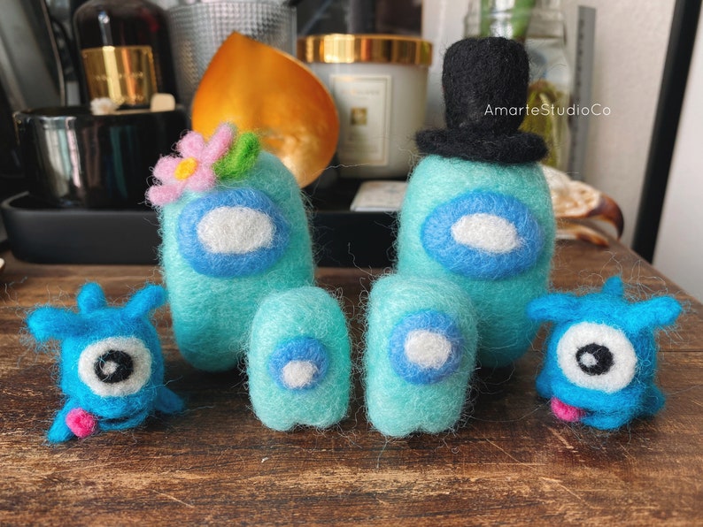 K&ouml;nnte beinhalten: Ein Set aus f&uuml;nf Filzspielzeugen, darunter zwei blaue Filzfiguren mit H&uuml;ten, eine blaue Filzfigur mit einer Blume und zwei kleinere blaue Filzfiguren. Die Figuren sind alle in Form einer Person mit einem runden Kopf und einem kleinen K&ouml;rper. Die Spielzeuge sind alle handgefertigt und haben ein skurriles, verspieltes Aussehen.