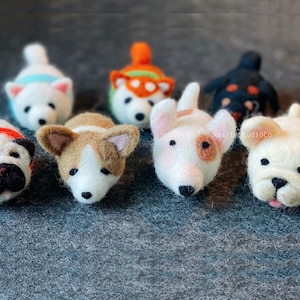 May include: A collection of eight felt animal figurines, each depicting a different breed of dog. The dogs are arranged in a row on a gray surface. The dogs are all white with different colored markings. The dogs are all looking at the camera.