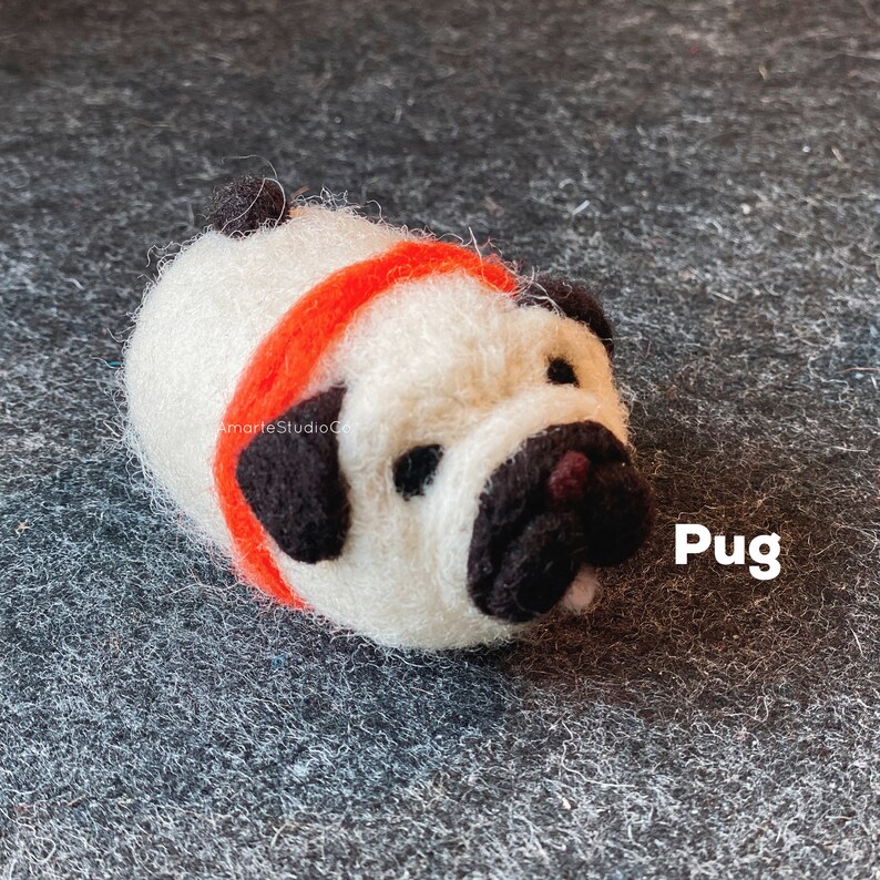 May include: A white felt pug with black ears and a black nose, wearing a red felt headband. The pug is lying on its side with its tongue sticking out. The word "Pug" is written in black text on a gray background.