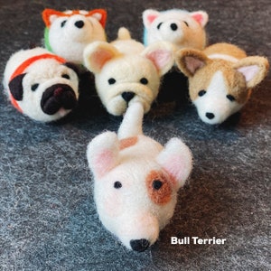 May include: A collection of felt animal figurines, including a pug, a French bulldog, a corgi, a husky, and a bull terrier. The bull terrier is white with brown spots and the text "Bull Terrier" is written below it.
