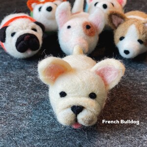 May include: A close-up of a white felt French Bulldog figurine with black eyes and a pink nose. The figurine is lying on its side with its tongue sticking out. The text "French Bulldog" is written below the figurine.