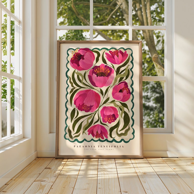 May include: Framed botanical illustration featuring a pink Paeonia tenuifolia, also known as the Fernleaf peony. The artwork showcases several pink flowers with detailed green foliage, set against a cream background within a scalloped teal border. The botanical name and common name are printed at the bottom. The print is displayed against a light wood floor near a window.