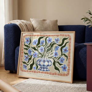Könnte beinhalten: Ein gerahmter rechteckiger Kunstdruck mit einer blau-weißen Vase im Harlekinmuster, gefüllt mit blauen Anemonen und grünen Blättern auf cremefarbenem Grund mit rosa gewelltem Rand und dem Text HARLEQUIN VASE WITH ANEMONE.