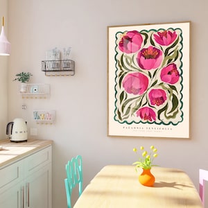 May include: Pink floral poster print featuring Paeonia tenuifolia, the fern-leaf peony, in a vintage style. The artwork showcases a cluster of vibrant pink flowers with green foliage, set against a cream background within a decorative border. The poster's dimensions are not specified, but it's displayed in a light-colored room with teal and pink chairs, a light-colored kitchen counter, and a small vase of yellow flowers.