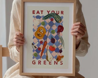May include: A framed print with a light blue and pink checkered background. The print features a variety of fruits and vegetables, including a pear, a carrot, a tomato, a squash, and a mushroom. The text "EAT YOUR GREENS" is printed in red at the top and bottom of the print.