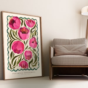 May include: A framed botanical illustration featuring pink Paeonia tenuifolia flowers with green leaves on a cream background. The artwork has a scalloped teal border and includes the text 'PAEONIA TENUIFOLIA' at the bottom. The print is displayed against a light beige wall, leaning against a light brown armchair with a checkered pattern.