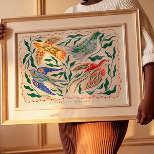 May include: A framed art print with a gold-toned frame, depicting vibrant birds and foliage. The artwork features birds in orange, blue, pink, and red, set against green leaves. The text "LES PETITS OISEAUX" is displayed at the bottom of the print.