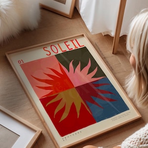 Könnte beinhalten: Ein gerahmter Kunstdruck mit dem Wort "SOLEIL" in Rot, über einem Sonnenmotiv, das in rote, rosa, grüne und blaue Quadranten unterteilt ist. Der Druck enthält den Text "PROVERBE 01" und "GARDEZ TOUJOURS VOTRE VISAGE VERS LE SOLEIL".