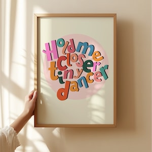 May include: A framed print with a pink circle and the text "Hold me closer tiny dancer" in colourful letters.
