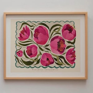May include: A framed floral print showcasing bright pink peonies with yellow centers and green foliage. The artwork is set against a cream background with a scalloped green border. The print is in a light wood frame, suitable for wall decor.