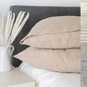 May include: Two beige linen pillowcases stacked on a gray headboard. The pillowcases are made of a soft, natural fabric and have a subtle texture.