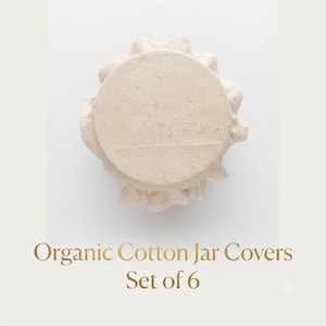 May include: A set of six round, off-white organic cotton jar covers with ruffled edges. The fabric has a textured, woven appearance. The text "Organic Cotton Jar Covers Set of 6" is printed in gold lettering below the fabric covers.