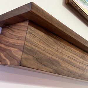 May include: A dark brown wooden shelf with a decorative edge. The shelf is mounted to a white wall.