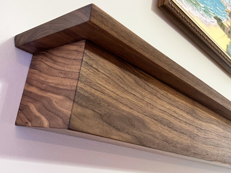 May include: A dark brown wooden shelf with a decorative edge. The shelf is mounted to a white wall.