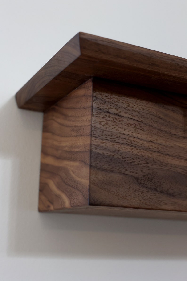 May include: A dark brown wooden shelf with a simple, rectangular design. The shelf has a slightly angled top edge and is made of solid wood with visible grain.