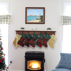 May include: A wood mantel with seven stockings hanging from it. The stockings are green with red and gold accents and have names embroidered on them. There is a wood-burning stove with a fire in it below the mantel. A blue armchair is to the right of the stove.