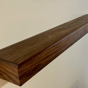 May include: A dark brown wooden shelf with a slightly rounded edge. The shelf is mounted to a white wall.