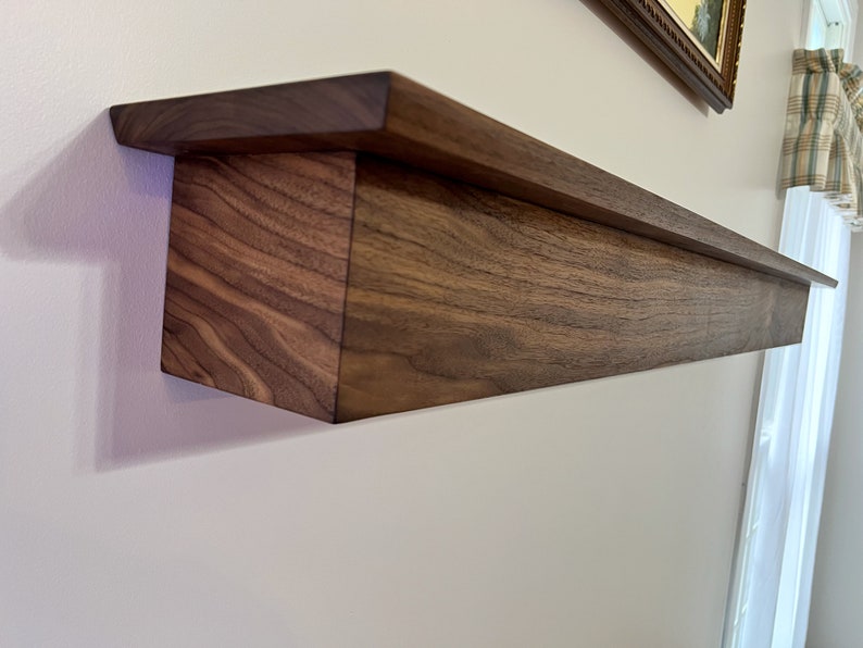 May include: A dark brown wooden shelf with a decorative edge, mounted on a white wall.