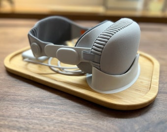 Può includere: Un'auricolare wireless bianca con una fascia grigia che riposa su un supporto in legno. L'auricolare ha un tessuto testurizzato che copre i padiglioni auricolari.