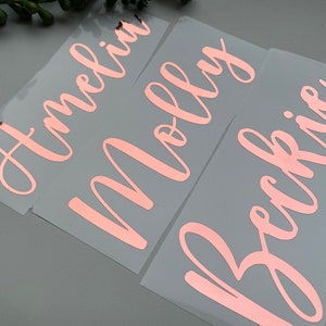 May include: Three individual adhesive vinyl decals featuring the names Amelia, Molly, and Beckie in a metallic rose gold script font. Each name is cut from a shiny, reflective material and presented on a clear, rectangular backing sheet.