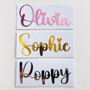 May include: Three rectangular white labels featuring custom names in cursive script. The top label displays the name Olivia in metallic pink with heart accents. The middle label shows Sophie in metallic gold. The bottom label features Poppy in black.