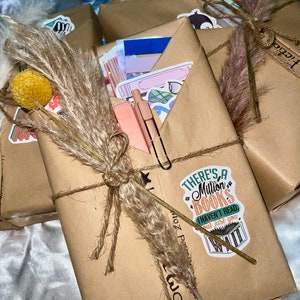 May include: A brown paper wrapped book with a sticker that says "There's a Million Books I haven't read but just you wait". The book is tied with twine and decorated with a dried grass sprig and a small yellow ball.