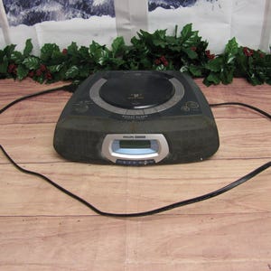 May include: A black Philips clock radio with a CD player and a digital display. The radio has a black power cord.