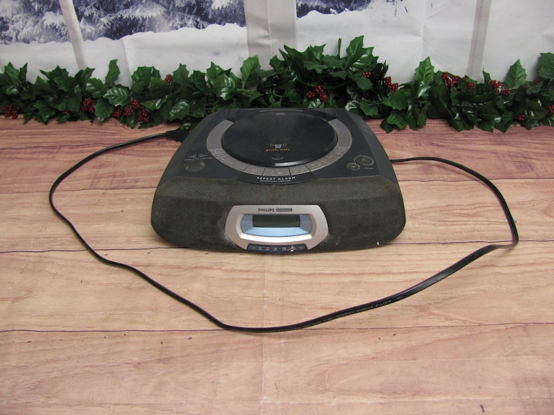 May include: A black Philips clock radio with a CD player and a digital display. The radio has a black power cord.